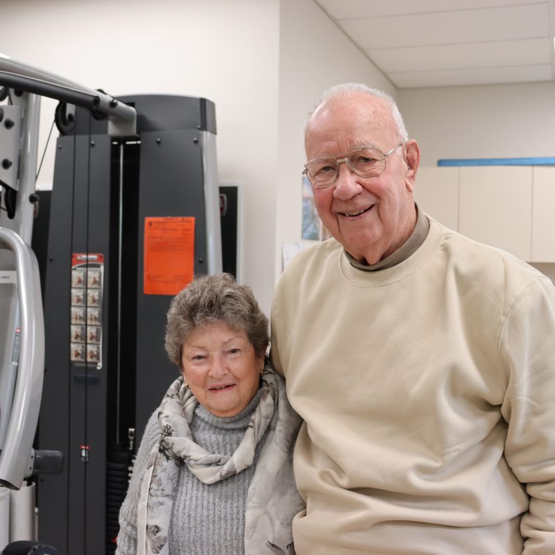 Husband and wife in their 80s smiling in a gym room